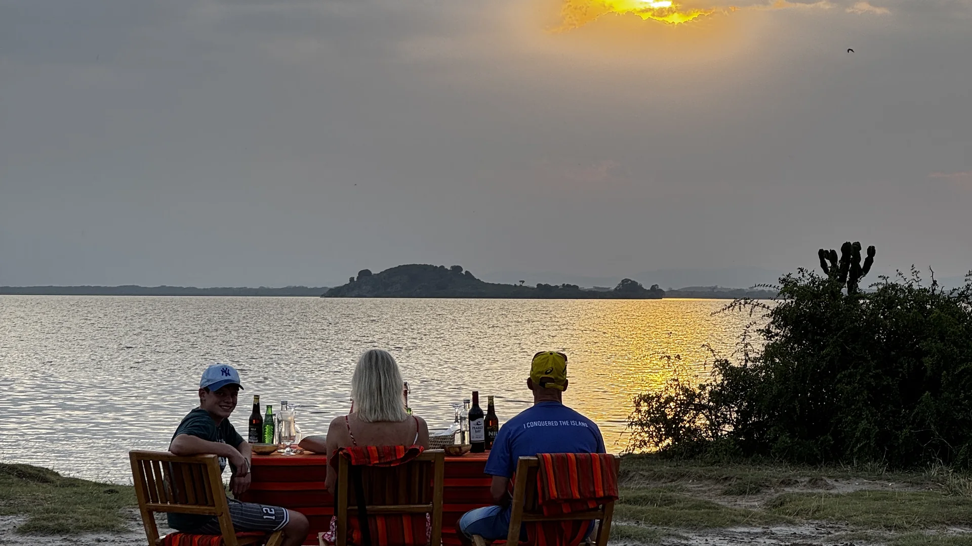 Guests enjoying sundowner drinks beside a lake at sunset on an Orika Africa safari in Uganda